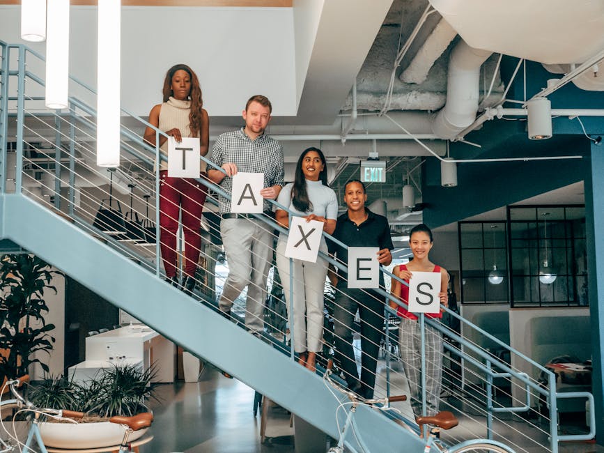 Multicultural business team holding 'Taxes' signs on a modern office staircase, symbolizing collaboration.